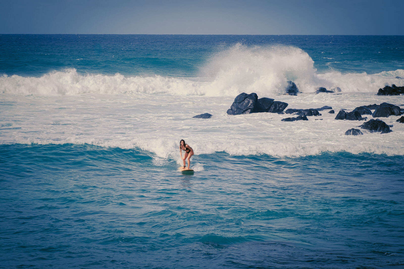 Surfer riding a wave off a lava rock coastline
