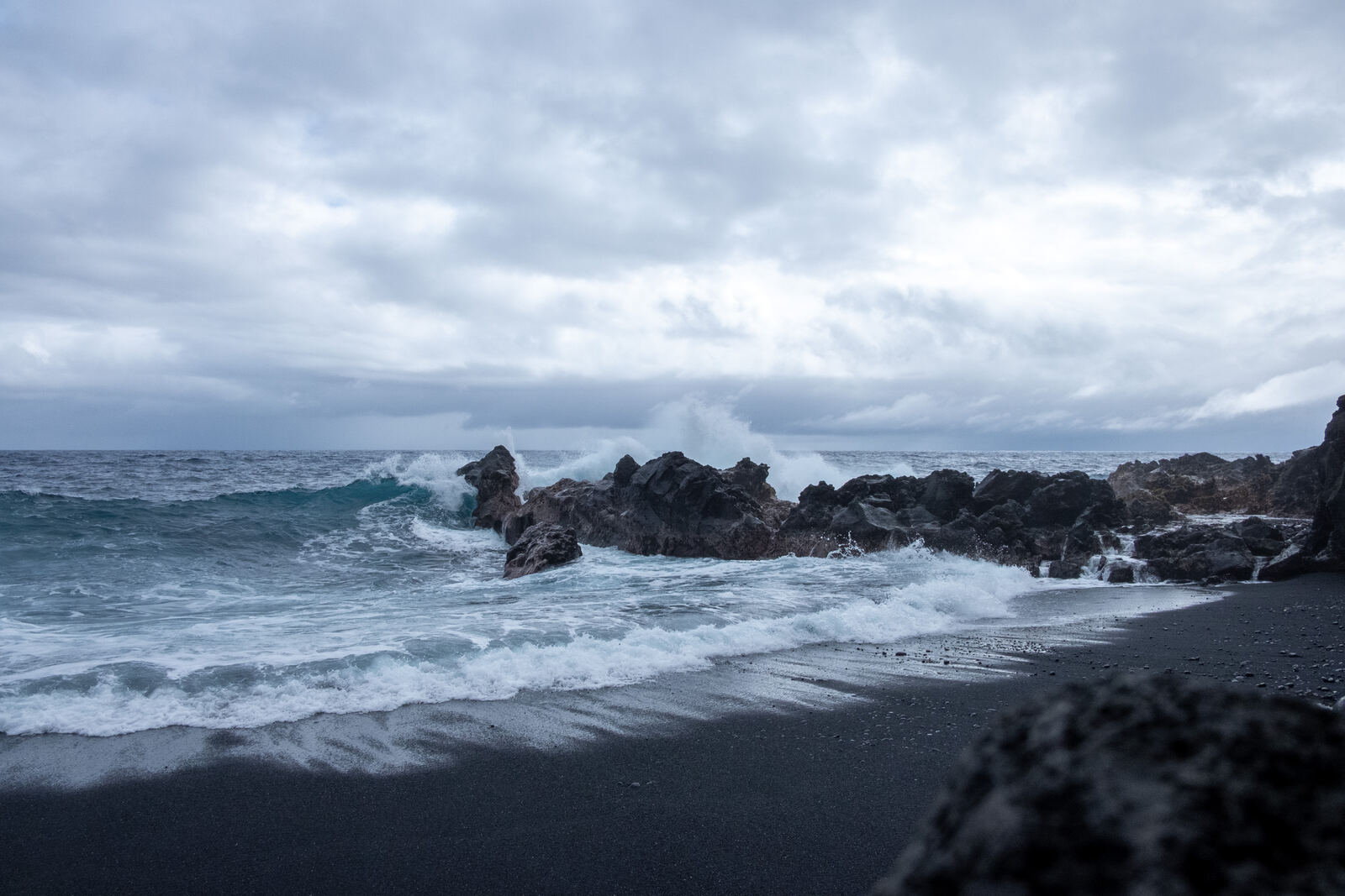 Storm surf breaking on black sand and lava rock